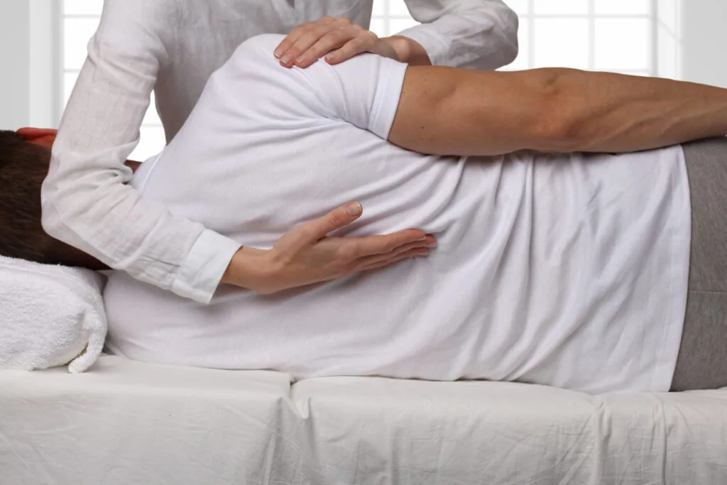 Healthcare provider performing manual examination of patient's leg and knee while patient lies on treatment table