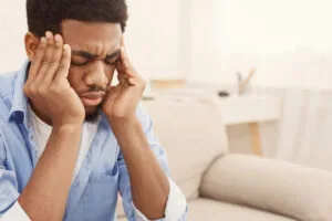 Man in blue shirt holding his head with both hands, eyes closed, appearing stressed or experiencing headache pain