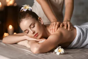 Woman receiving a back massage from a therapist in a spa setting with candles and white flowers