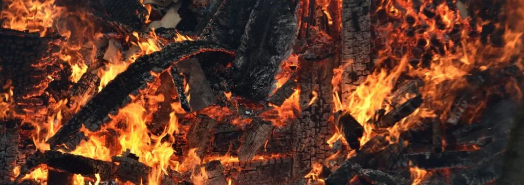 Intense orange and yellow flames consuming dark charred wood logs