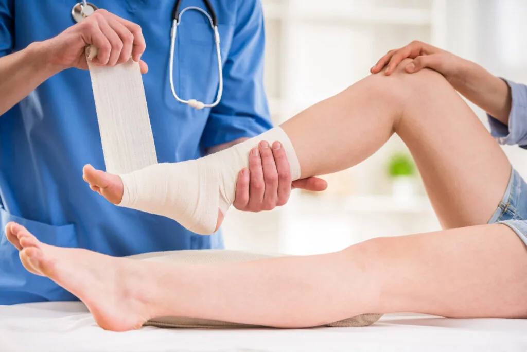 Healthcare provider wrapping white bandage around patient's ankle and foot