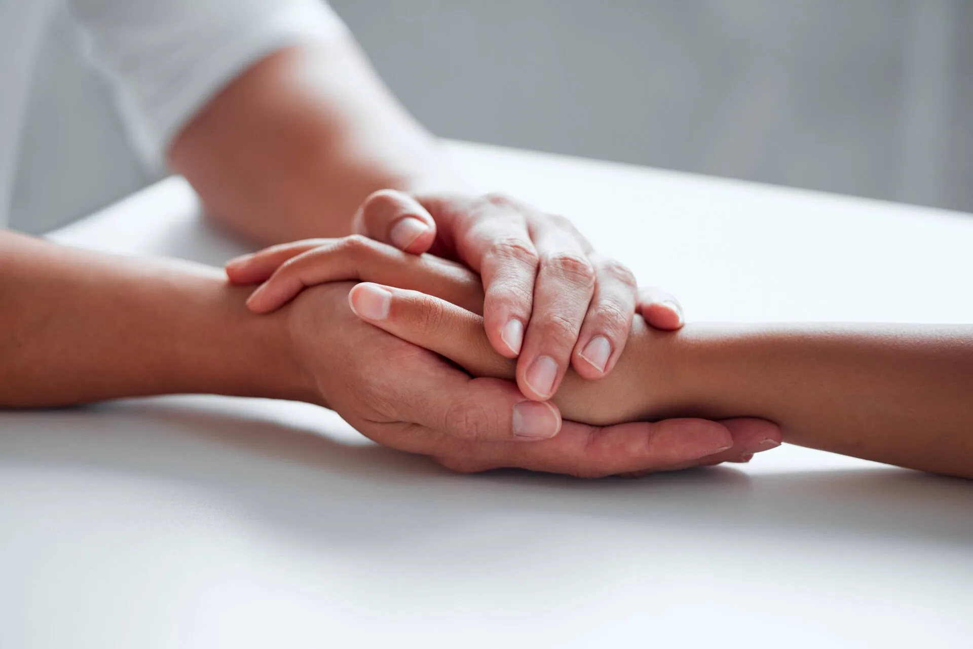 Multiple hands stacked together on a white surface in a gesture of unity and support