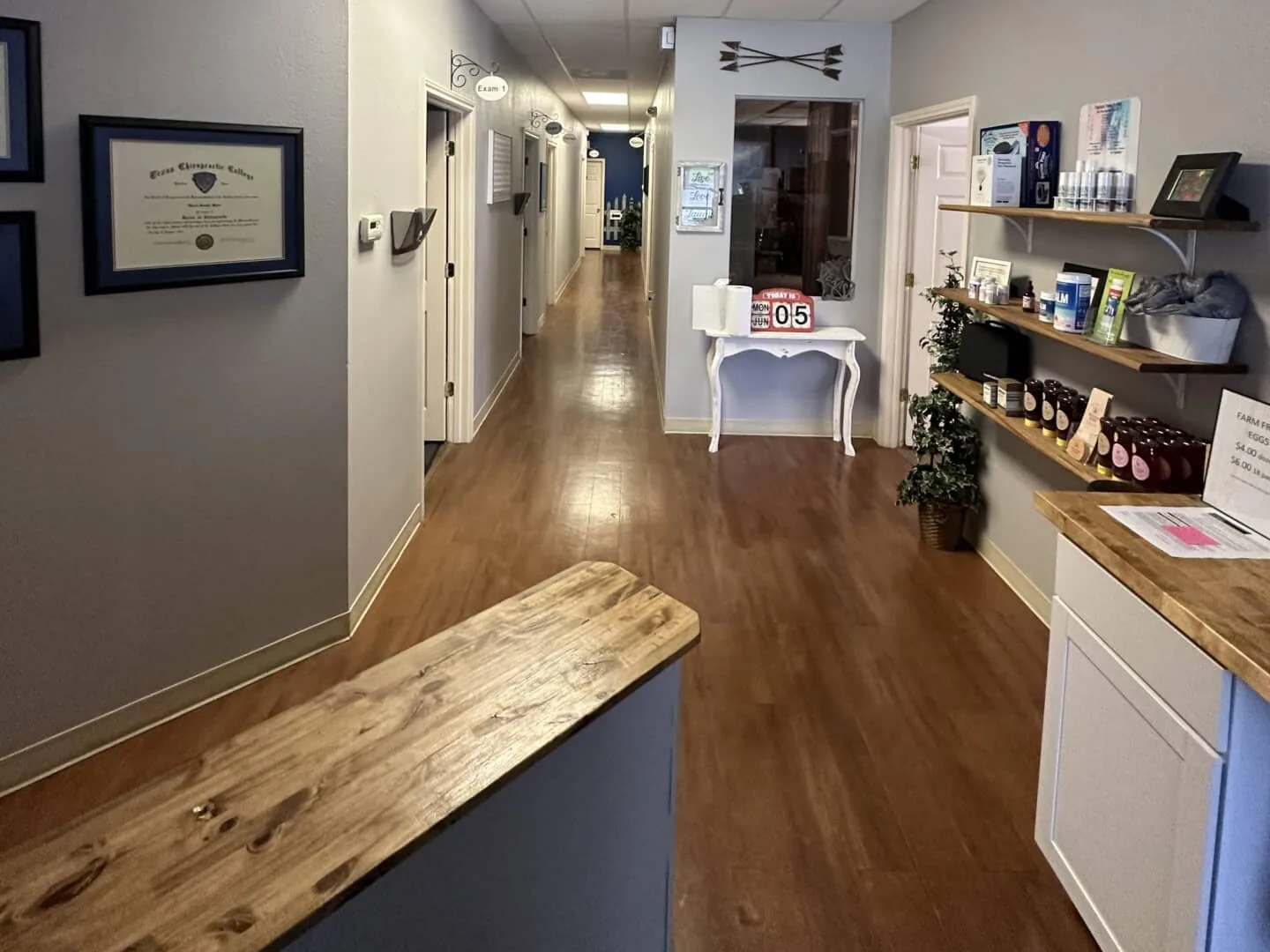 Modern medical office front desk with wooden counter, shelving with products, and hallway leading to treatment rooms