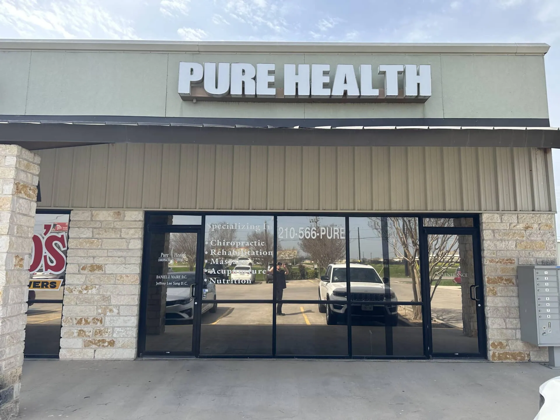 Pure Health storefront with tan and stone exterior, black-framed glass doors and windows, white signage on building facade